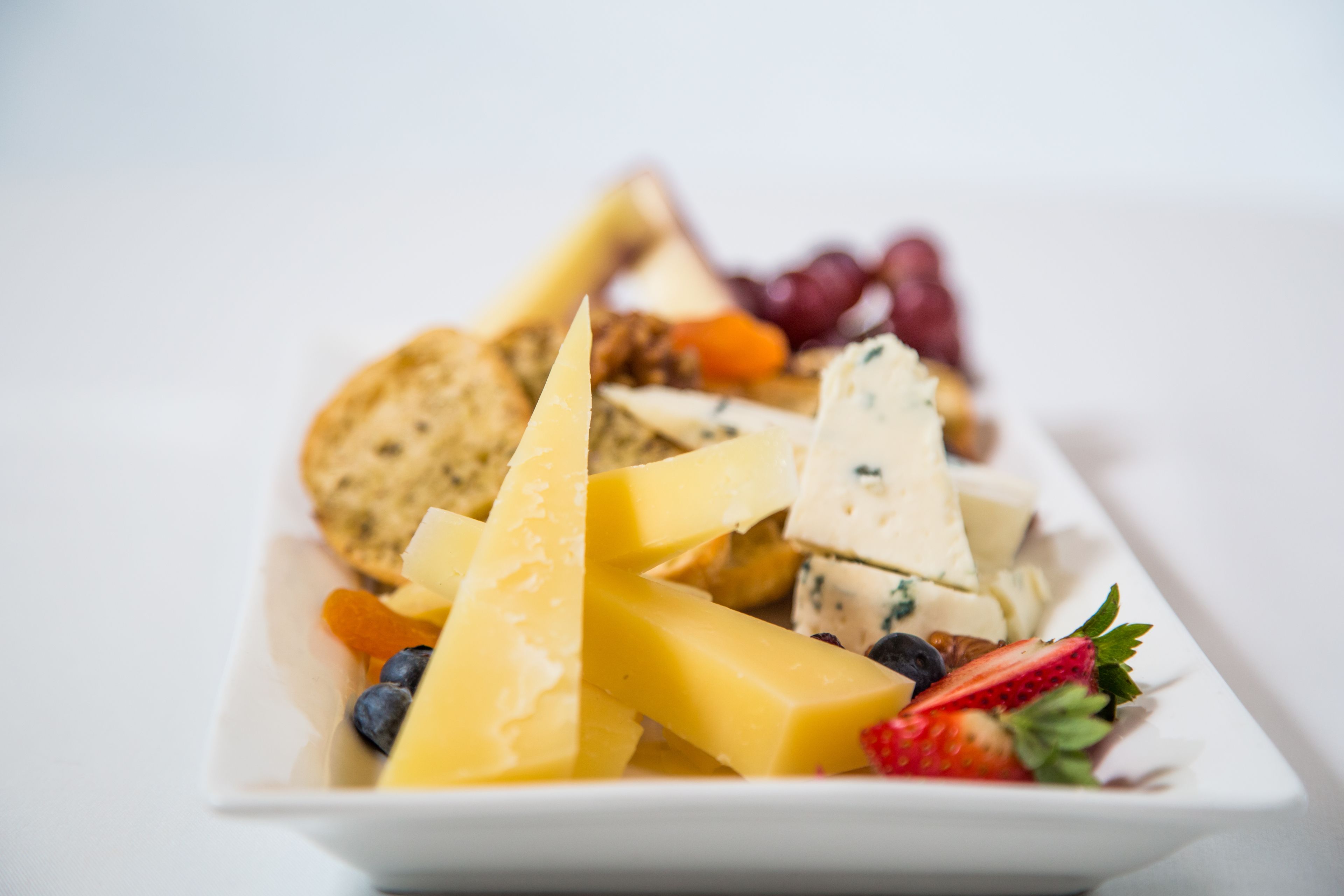 Une assiette rectangulaire blanche sur laquelle on trouve divers fromages, des crackers, des raisins et des fraises.