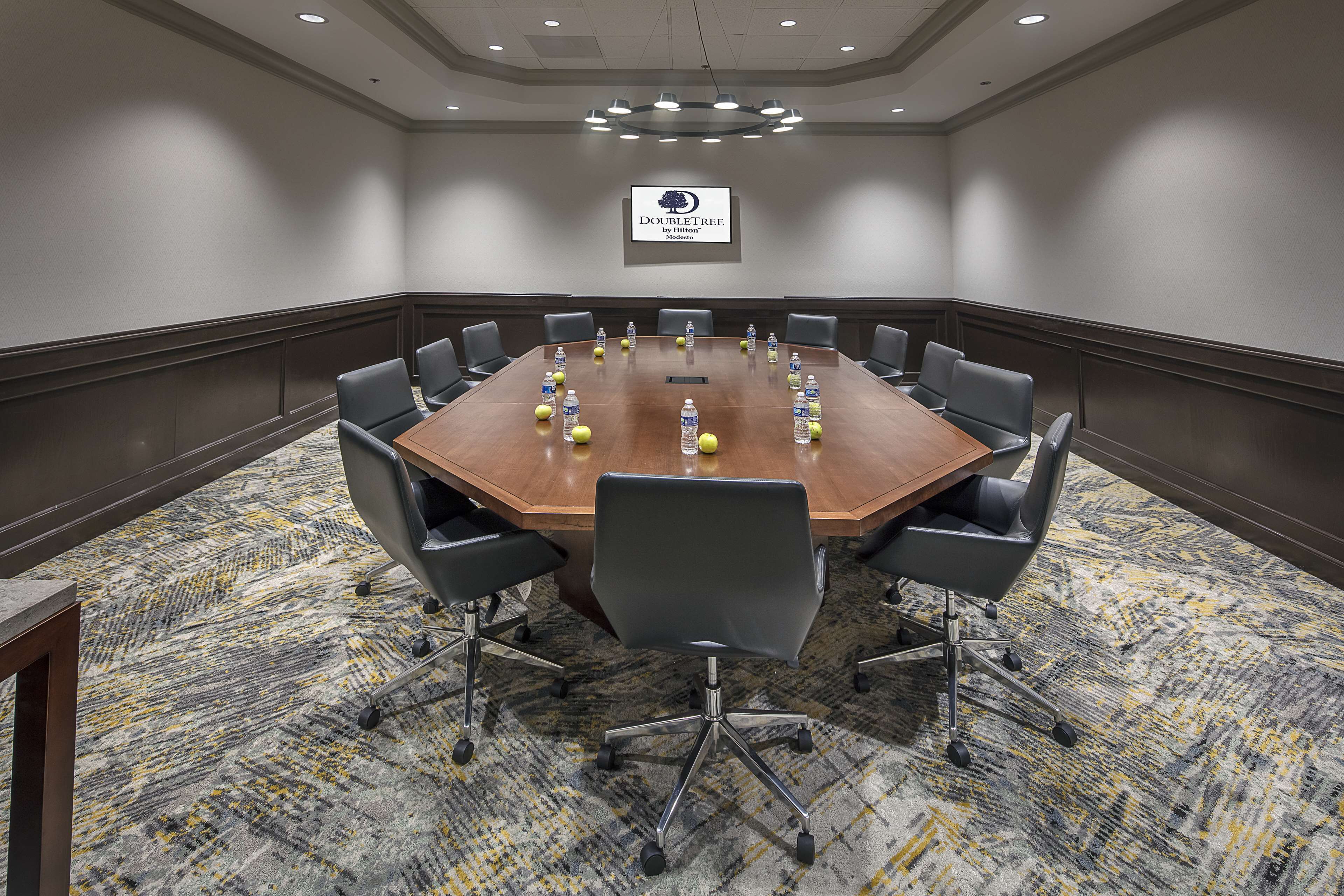 A conference room with a large wooden table, black chairs, and a carpeted floor.