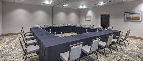 Un salón de conferencias con una larga mesa, sillas, botellas de agua y piso alfombrado.