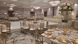 A spacious banquet hall with round tables, gold chairs, and elegant chandeliers.