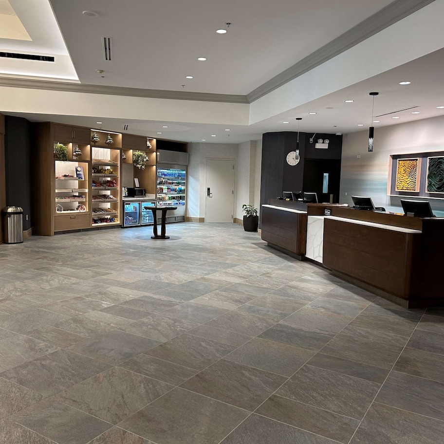 A spacious lobby with a reception desk, a self-service kiosk, and a refrigerated display.