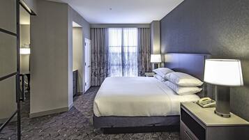 Quarto de hotel com uma cama grande, mesa de cabeceira com abajur, telefone e vista para árvores pela janela.