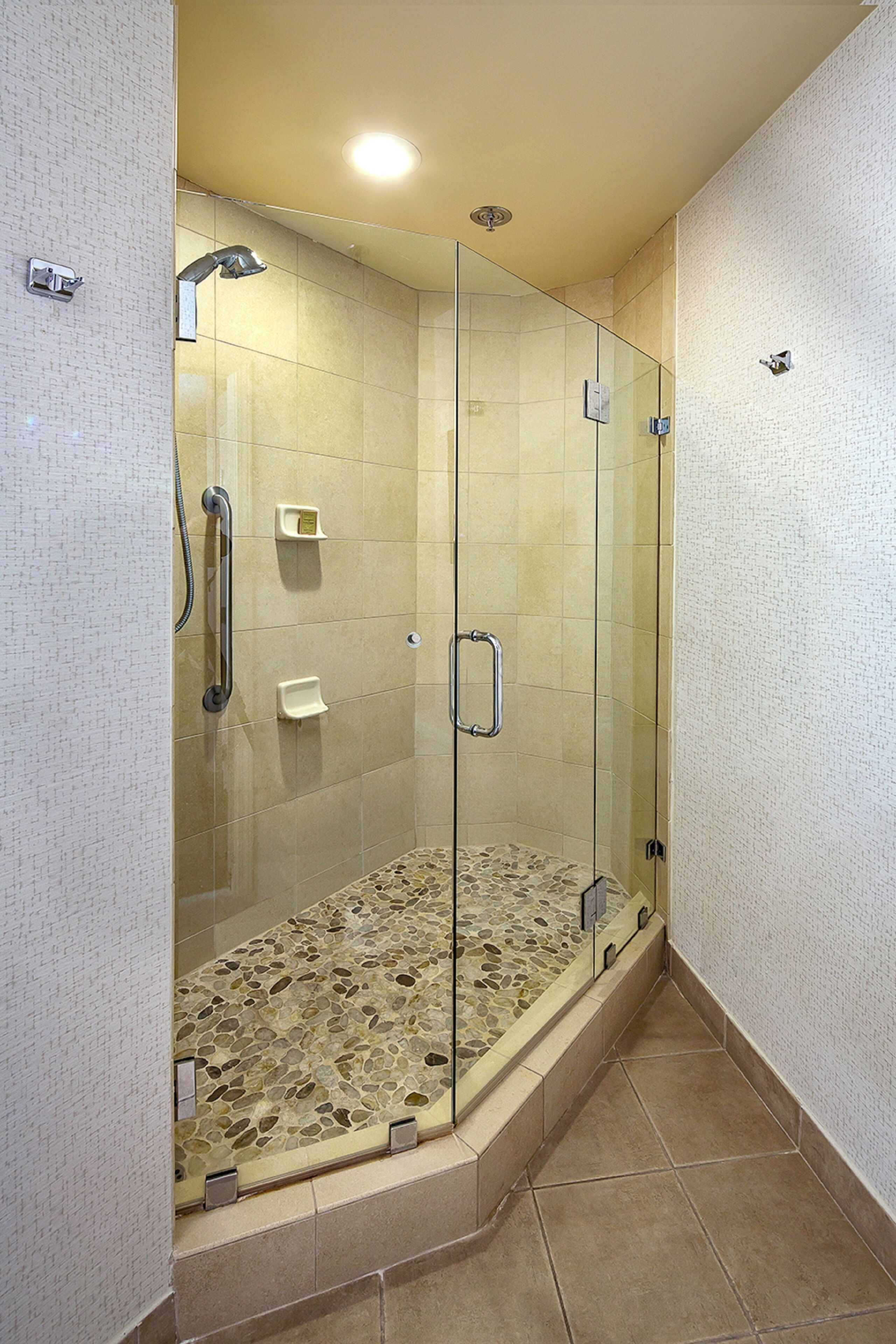 Een douche met glazen wanden, een betegelde vloer en een handgreep.