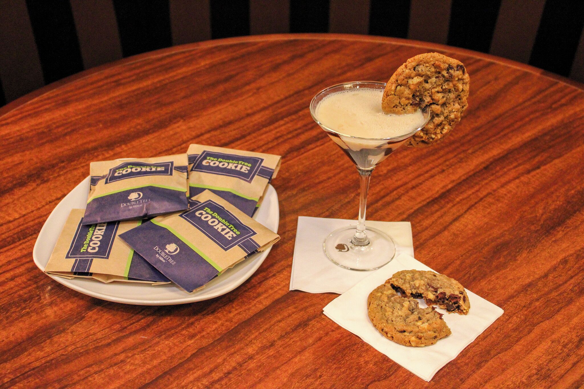 A plate of cookies, a glass of milk, and a cookie in a martini glass on a wooden table.