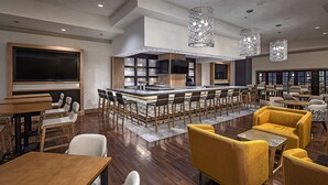 A modern bar area with a long counter, multiple bar stools, and a television screen.