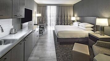 Una habitación de hotel moderna con cocina, una cama grande con cabecera, un escritorio y una silla.