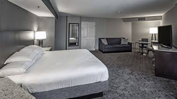 A hotel room with a large bed, a sofa, a desk with a TV, and a mirror.