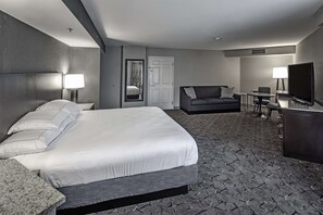 A hotel room with a large bed, a sofa, a desk with a TV, and a mirror.