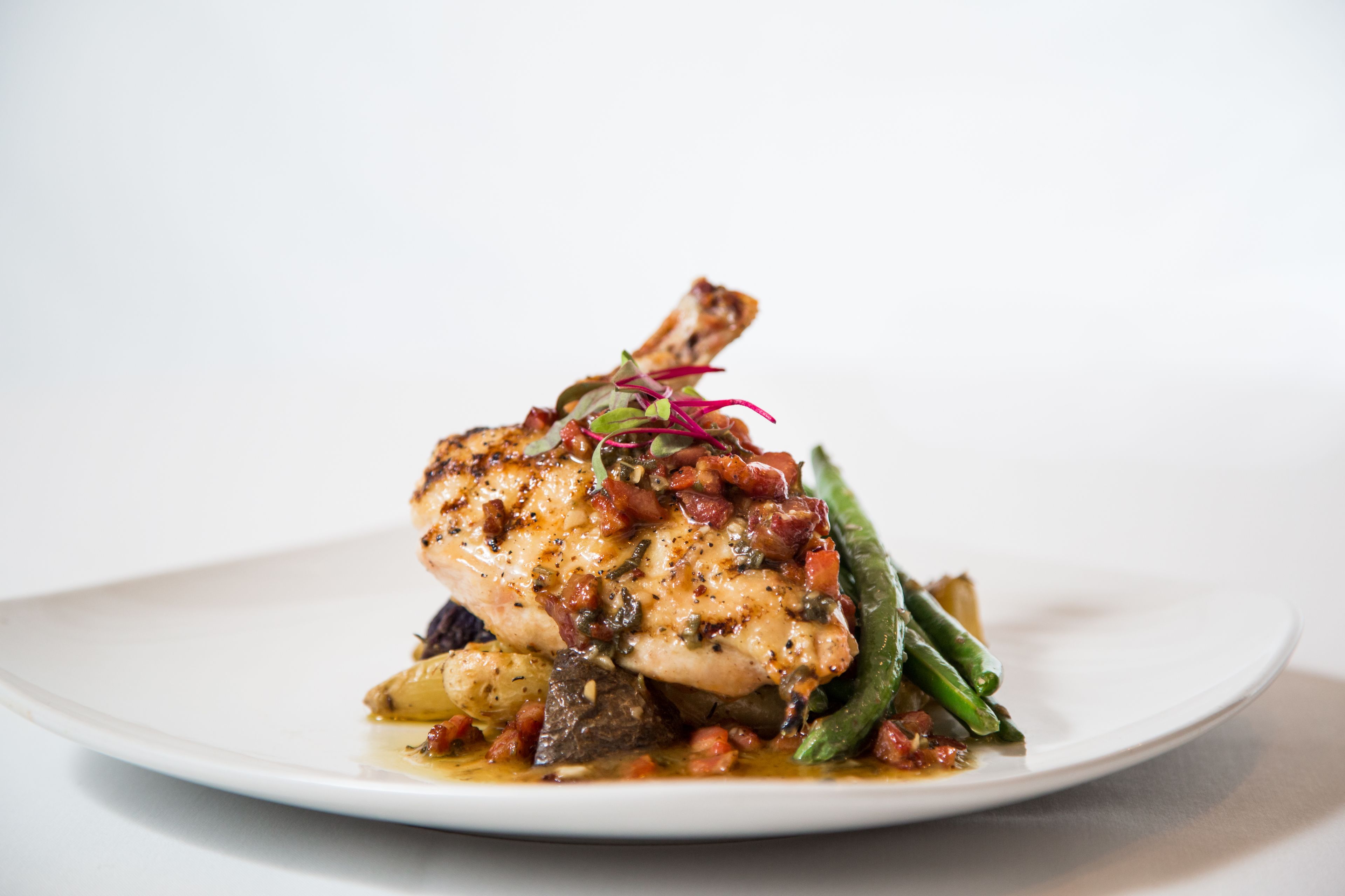 Une assiette contenant un morceau de poulet grillé, des haricots verts et une garniture de légumes rouges et verts.