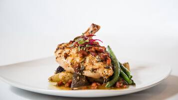Une assiette contenant un morceau de poulet grillé, des haricots verts et une garniture de légumes rouges et verts.