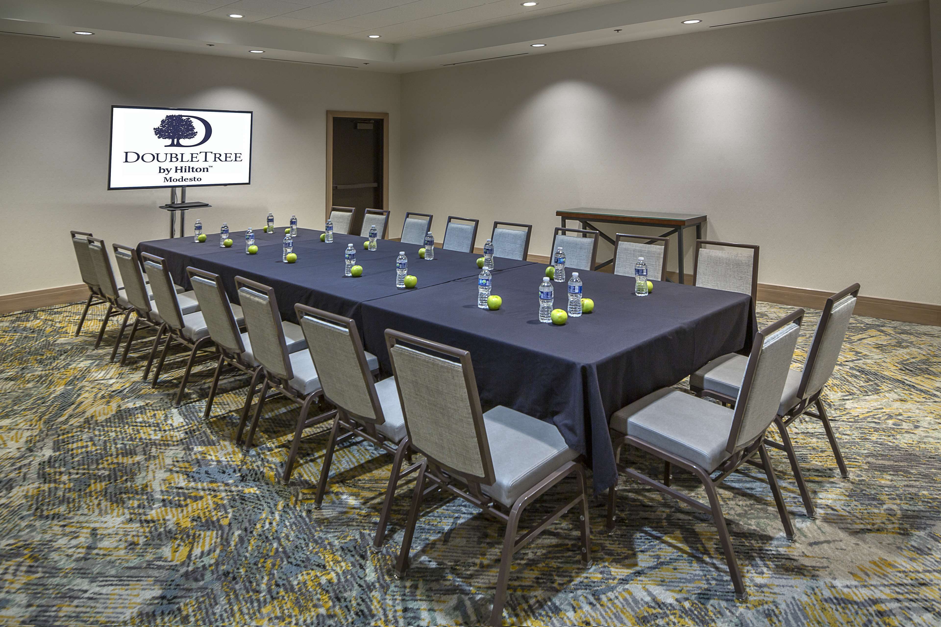 A conference room with a long table, chairs, water bottles, and a sign on the wall.