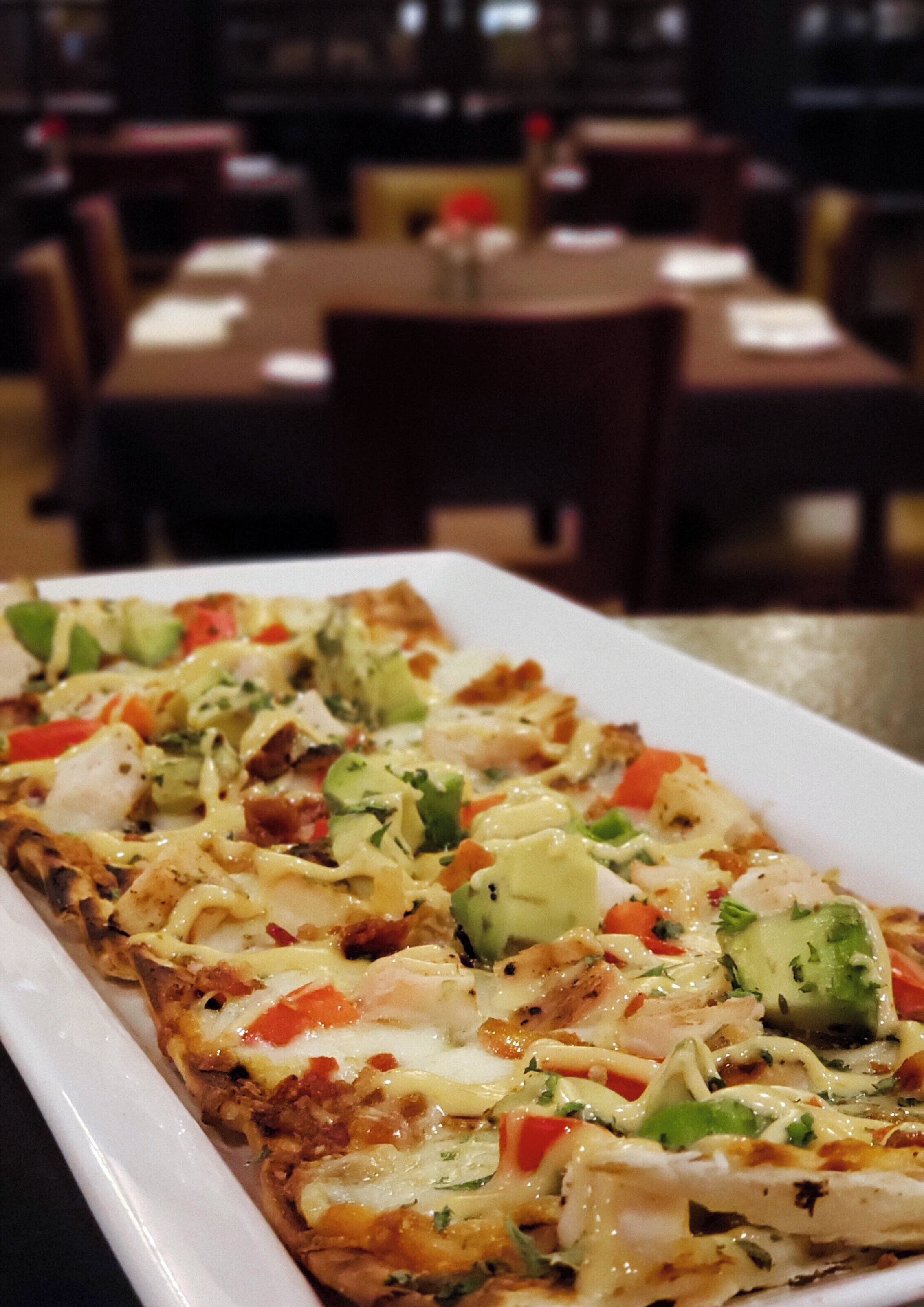 Prato retangular branco com pizza coberta de queijo, frango e vegetais.