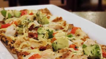 Prato retangular branco com pizza coberta de queijo, frango e vegetais.