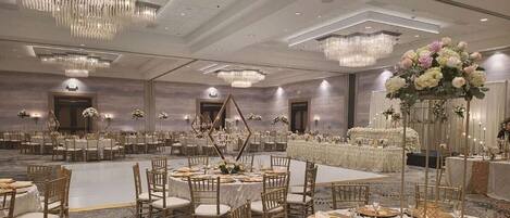 Un amplio salón de banquetes con mesas redondas, candelabros y centros de mesa florales.