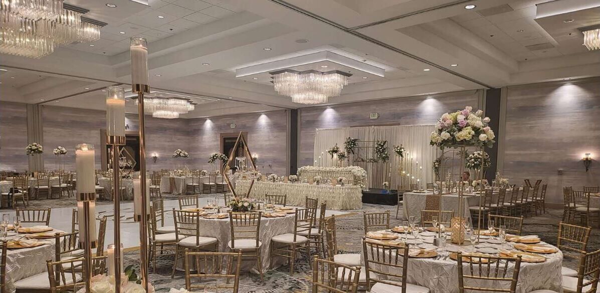 A banquet hall with round tables, gold chairs, and floral centerpieces.