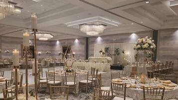 A banquet hall with round tables, gold chairs, and floral centerpieces.