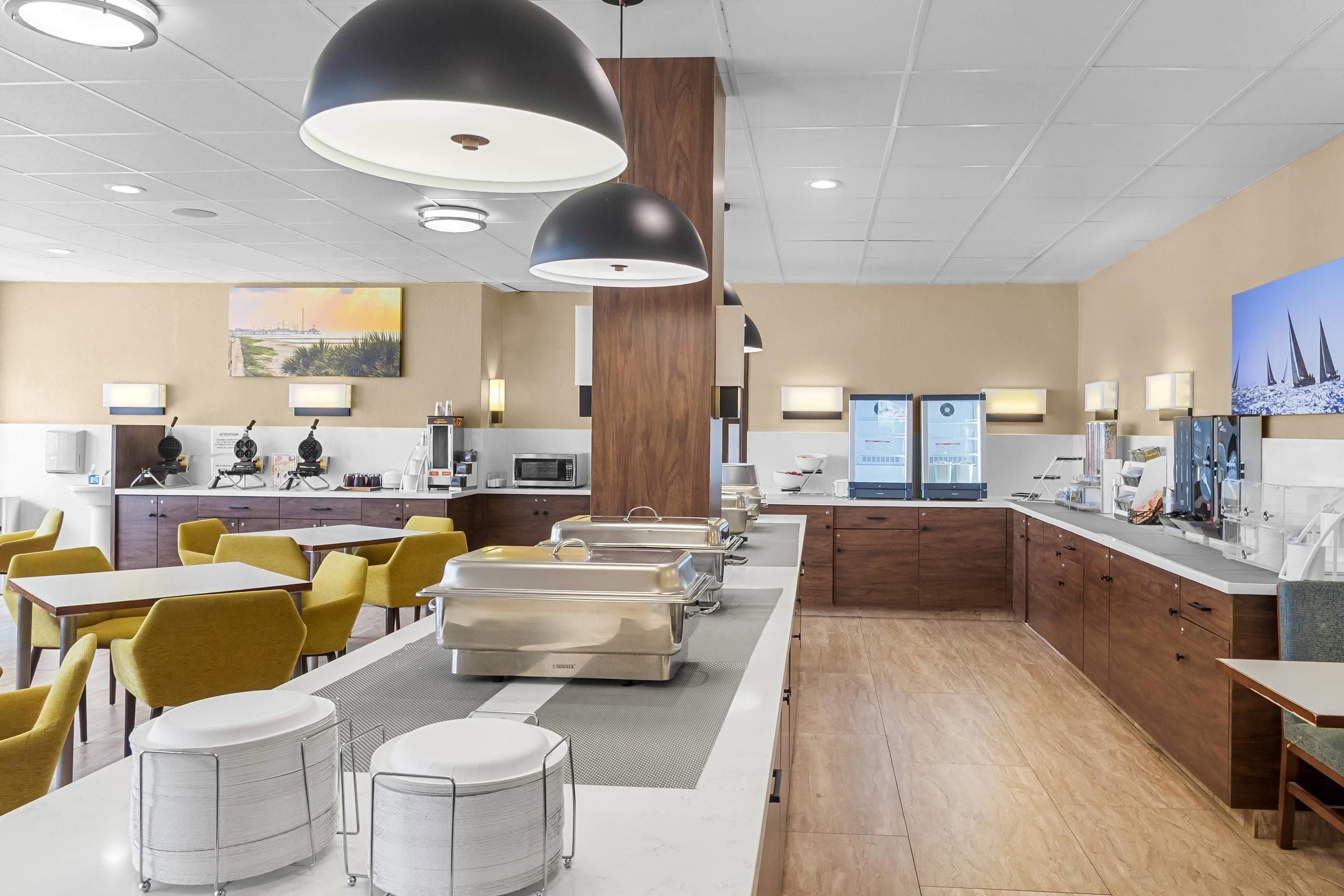 A modern hotel lobby with a dining area, kitchenettes, and artwork on the walls.