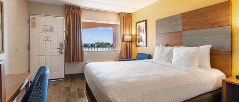 A hotel room with a large bed, a desk, a chair, a window with curtains, and a view of the outdoors.