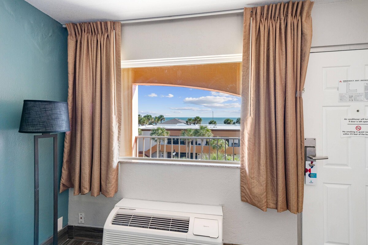 A room with a window, curtains, an air conditioning unit, a door with a sign, and a lamp.