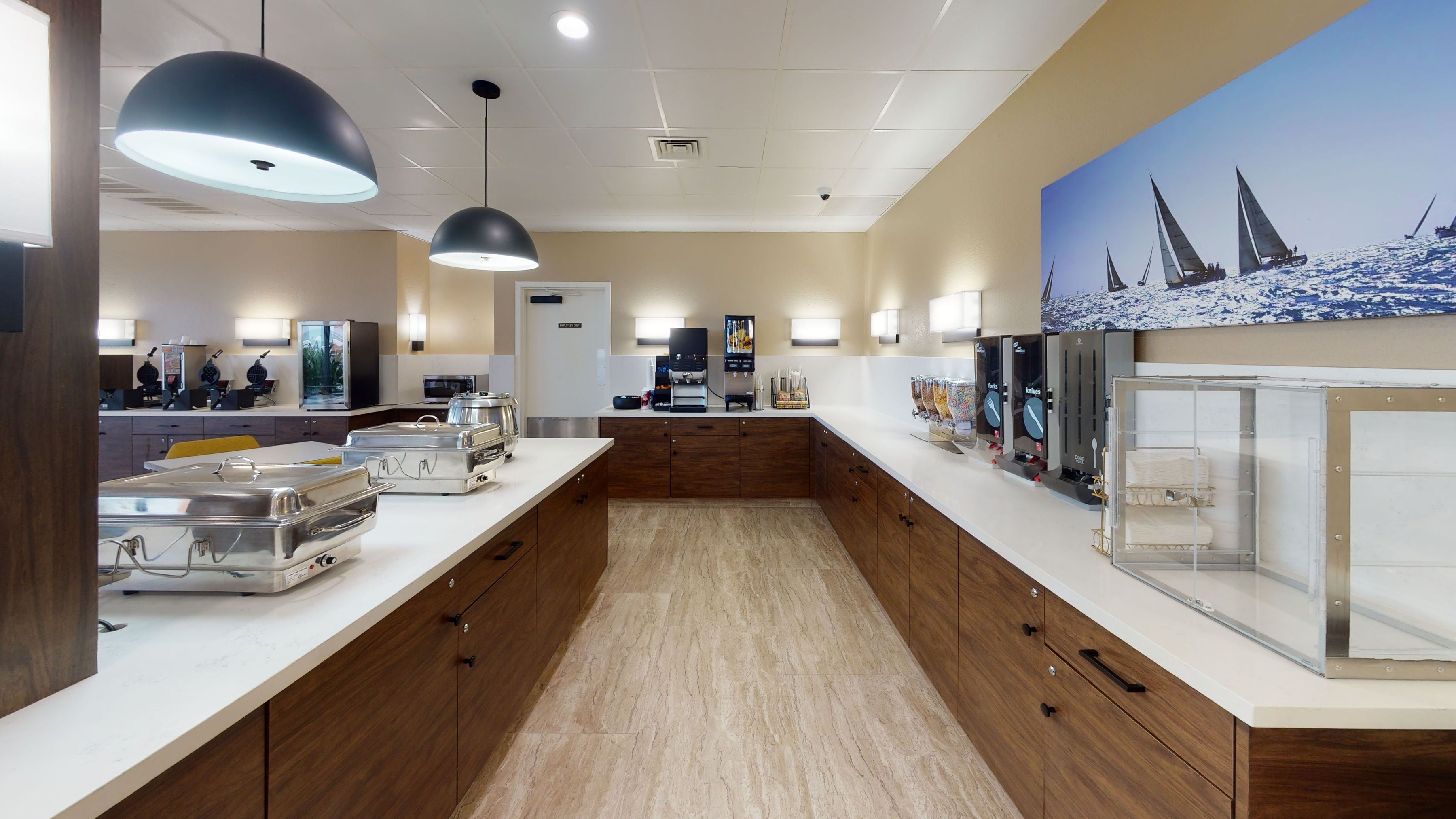 A modern hotel lobby with a long reception counter, buffet area, and a painting of sailboats on the wall.