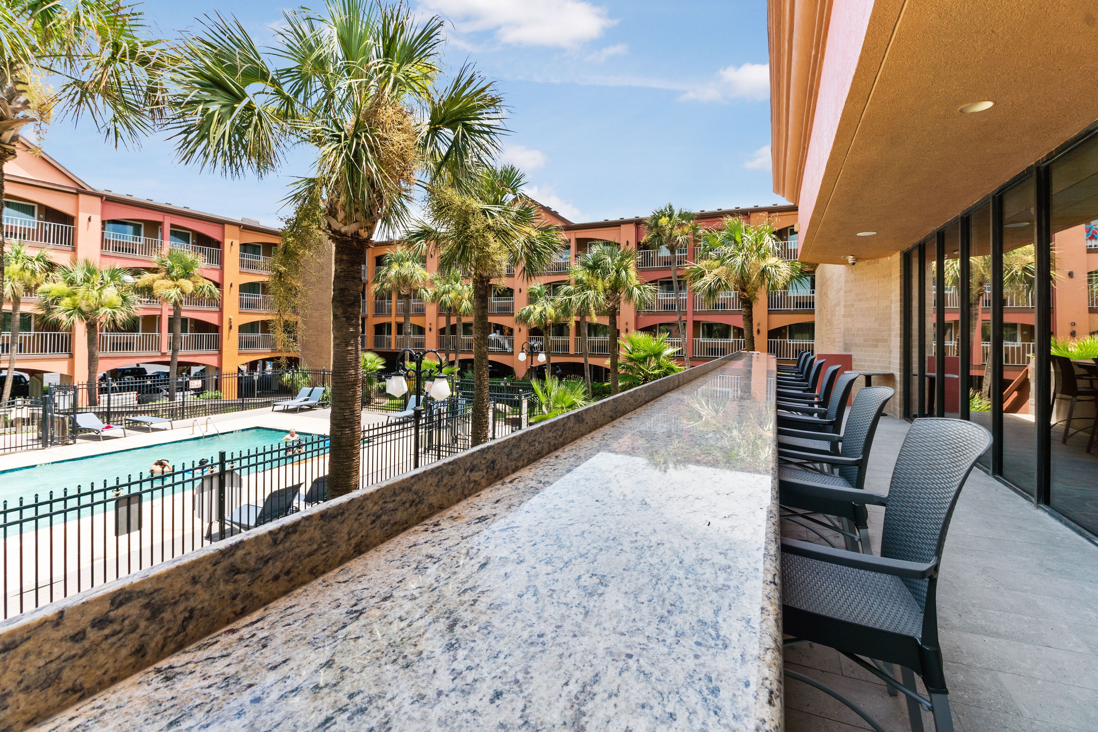 A hotel with a pool, outdoor seating, and palm trees.