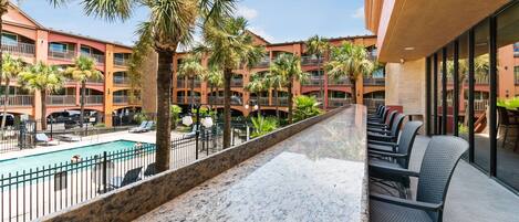 A hotel with a pool, outdoor seating, and palm trees.