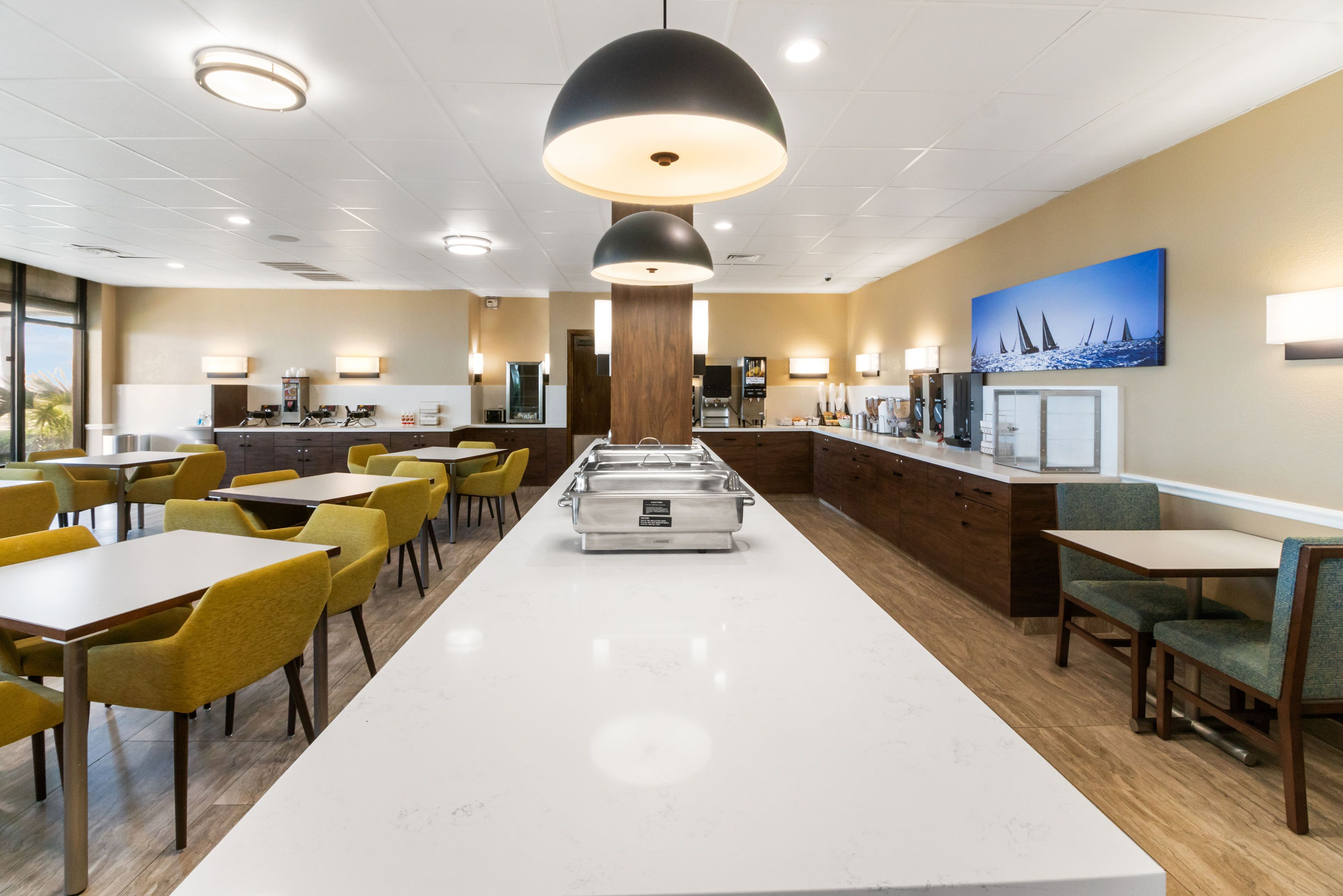 Un vaste espace dédié à la salle à manger, avec un long comptoir blanc, des chaises jaunes et un buffet central.