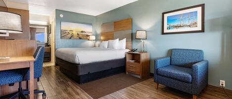 Ein Hotelzimmer mit Bett, Schreibtisch, Stuhl und einem gerahmten Bild an der Wand.