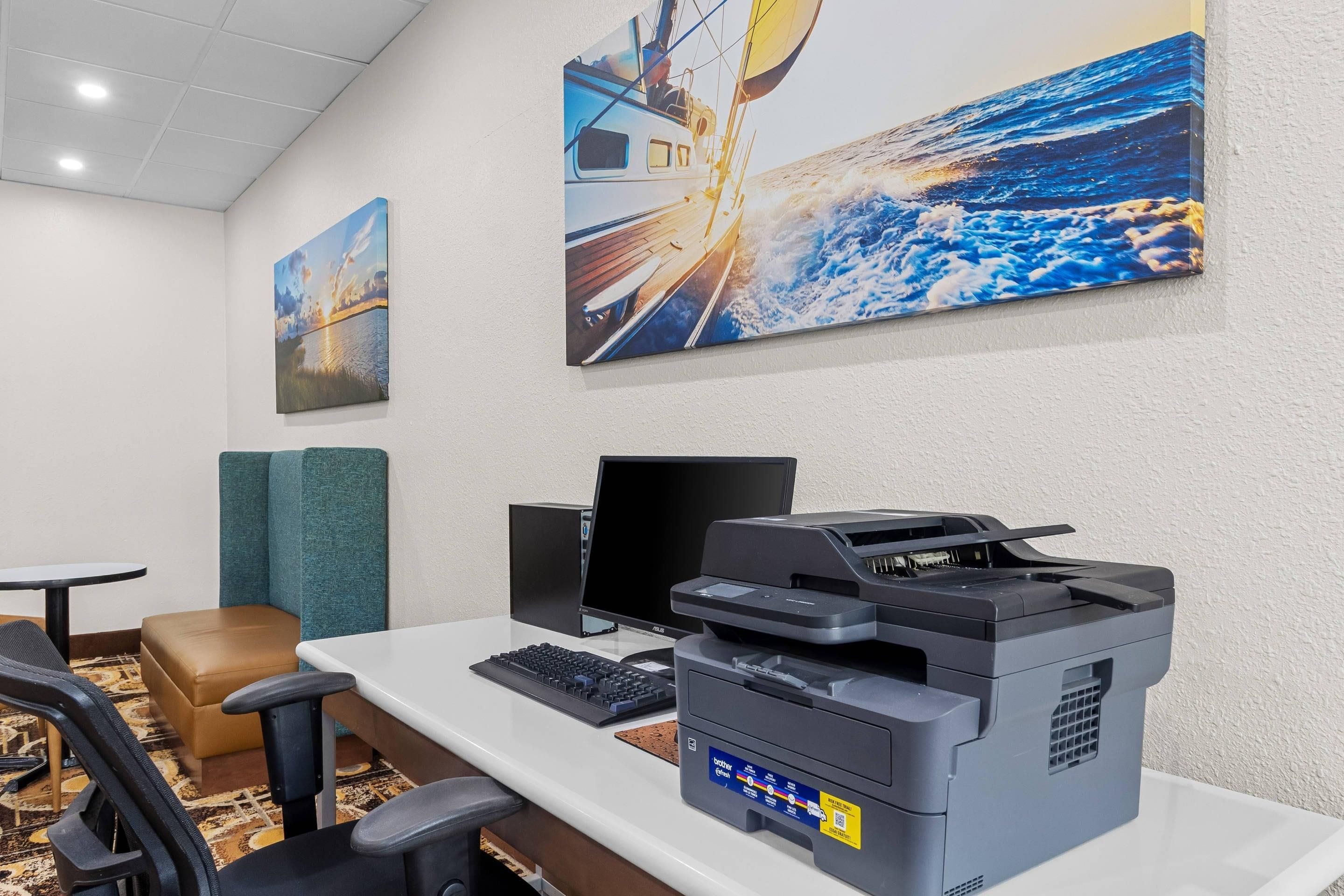 Una habitación de hotel con escritorio, computadora e impresora. Hay dos cuadros en la pared.