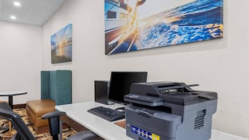 Una habitación de hotel con escritorio, computadora e impresora. Hay dos cuadros en la pared.