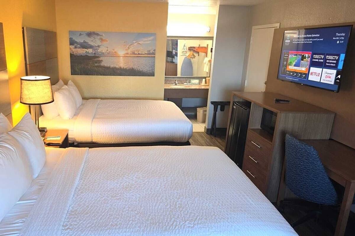 Een hotelkamer met twee bedden, een bureau, een televisie en een schilderij aan de muur.