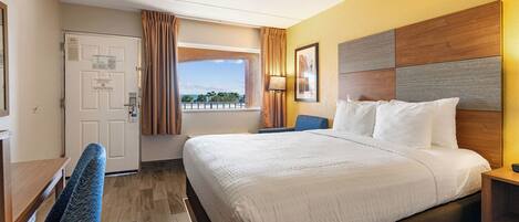 A hotel room with a large bed, a desk, a chair, a window with curtains, and a view of the outdoors.