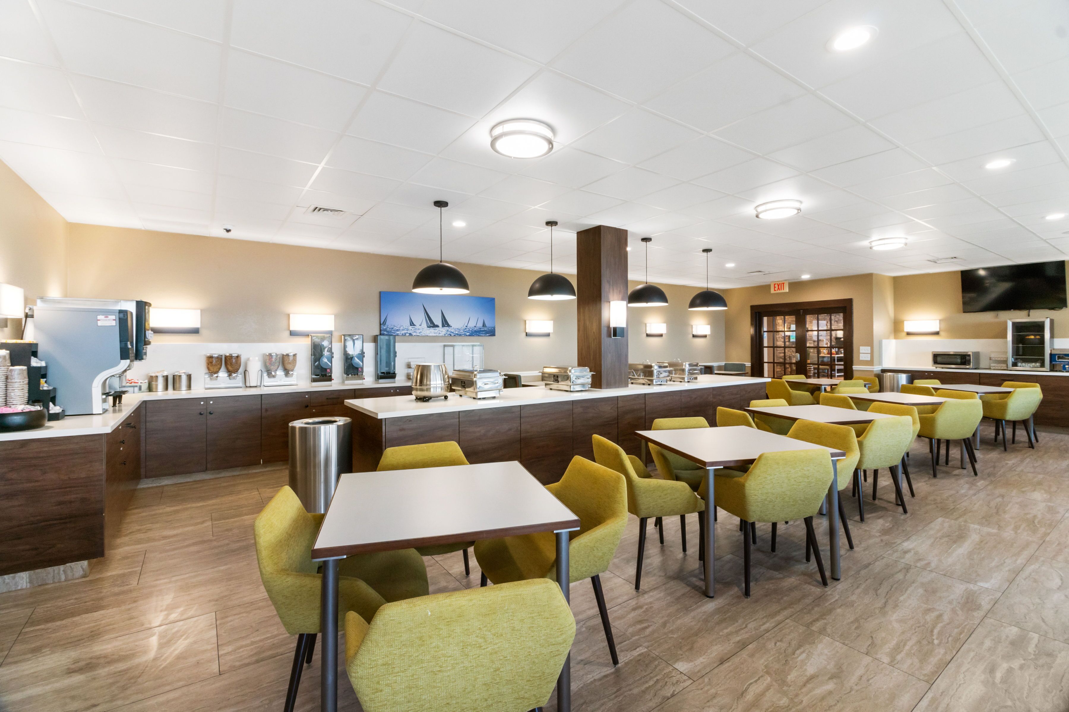 A modern restaurant with a long counter, yellow chairs, and a TV mounted on the wall.