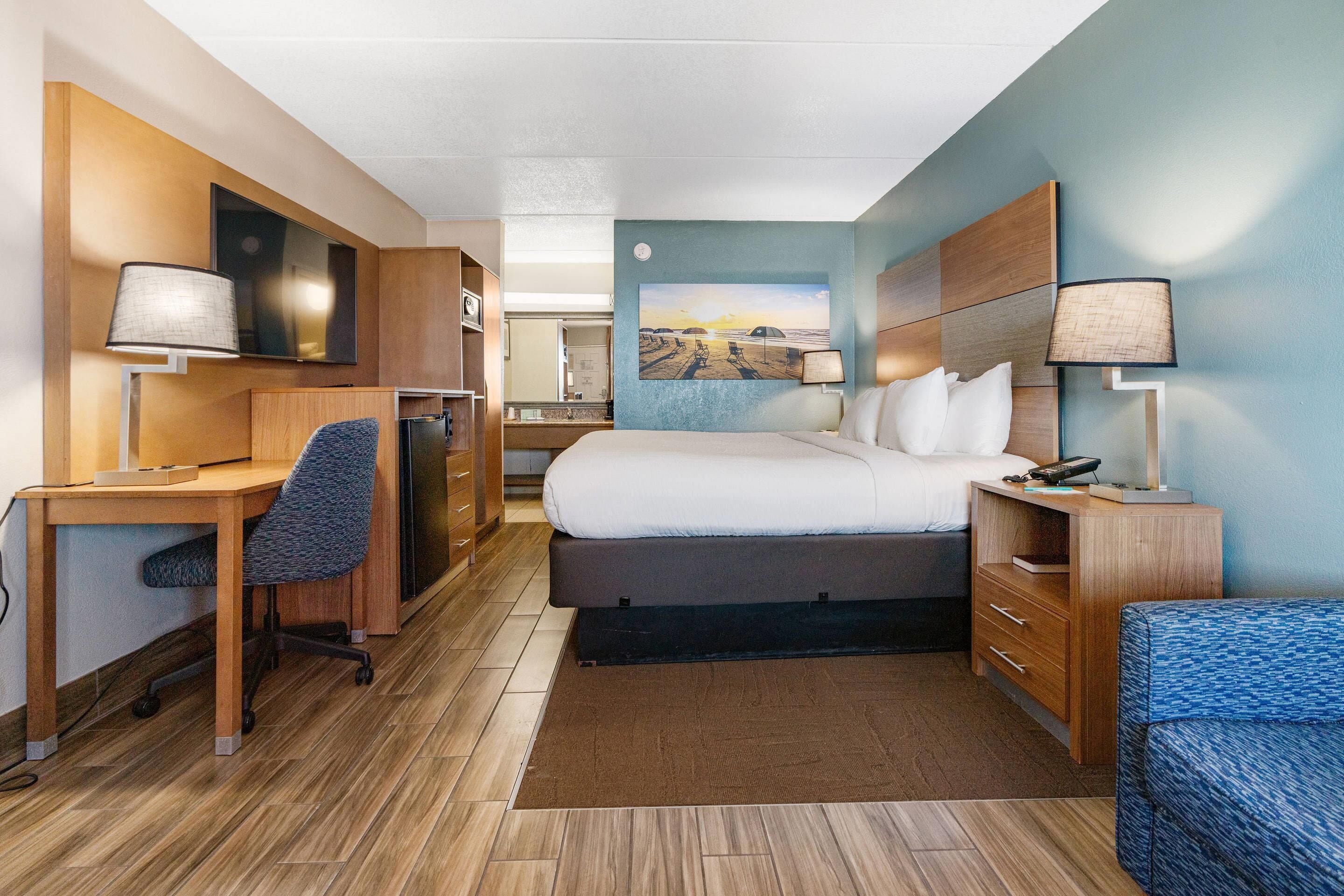 Une chambre d’hôtel avec un lit, un bureau, une chaise et un tableau au mur.