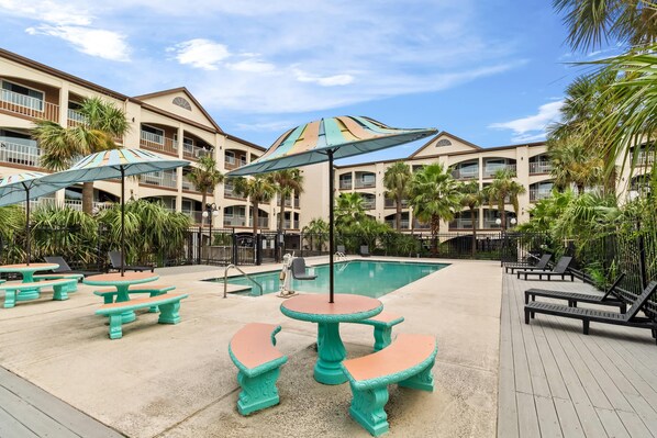 Un resort con mesas al aire libre, piscina y un edificio de varios pisos con balcones.