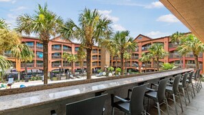 A hotel with a long bar area, outdoor seating, and palm trees.