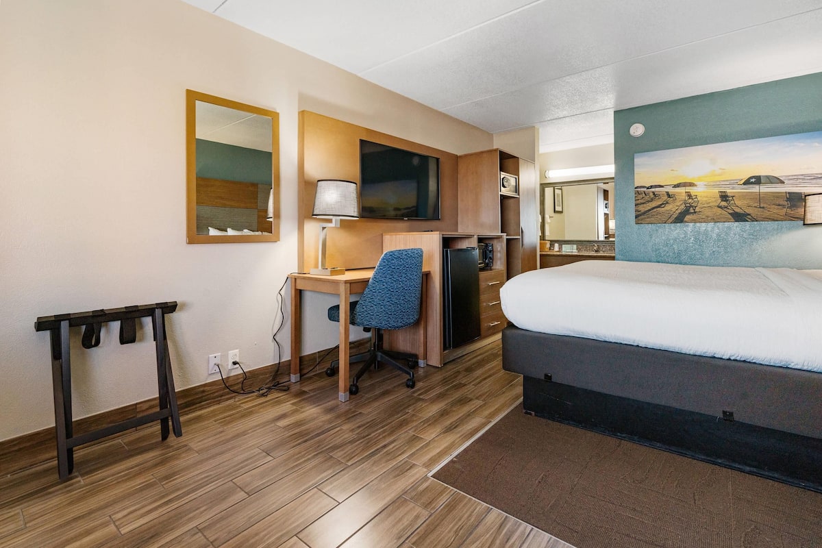 Een hotelkamer met een bed, bureau, stoel en een schilderij aan de muur.