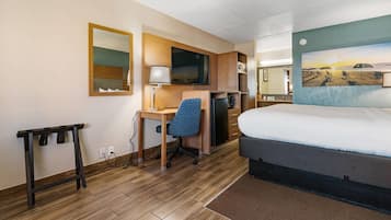 A hotel room with a bed, desk, chair, and a painting on the wall.