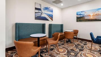Un hall de hotel con disposiciones para sentarse, incluyendo cabinas y sillas, y dos cuadros en las paredes.