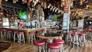 Zona de bar con taburetes de madera, una barra y diversas decoraciones, incluyendo calaveras y cuernos de animales.