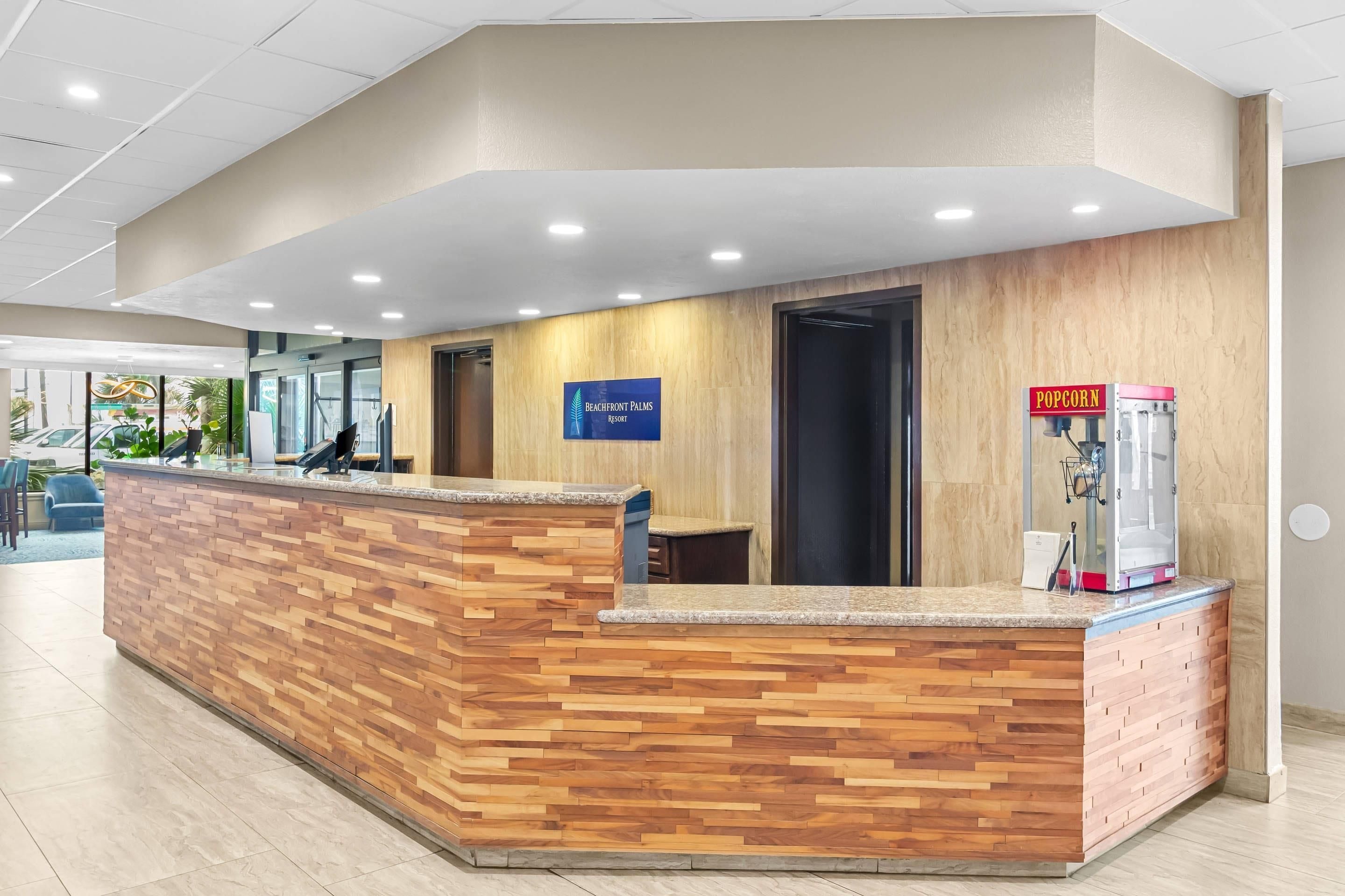 A reception desk with a wooden finish, a sign for Beachfront Palms Resort, and a popcorn machine.
