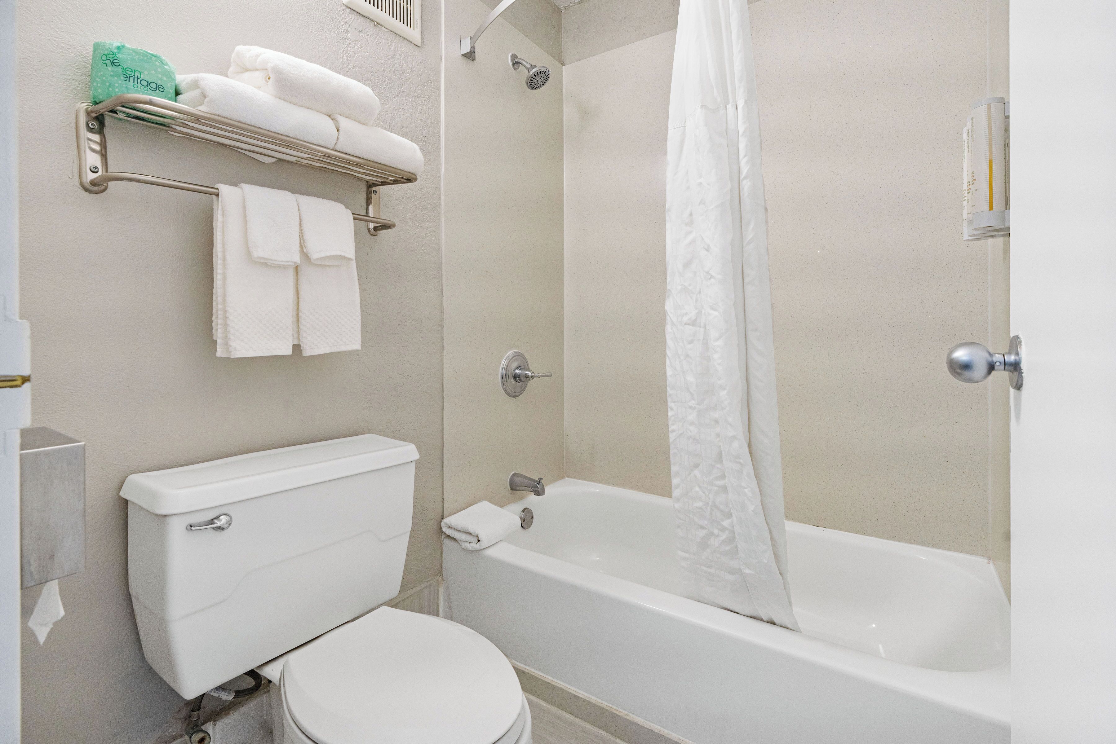 A bathroom with a toilet, a bathtub, a shower, and a towel rack with folded towels.