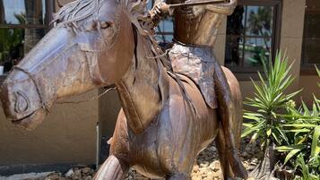 A bronze statue of a person on horseback in front of a building with a corrugated metal roof.