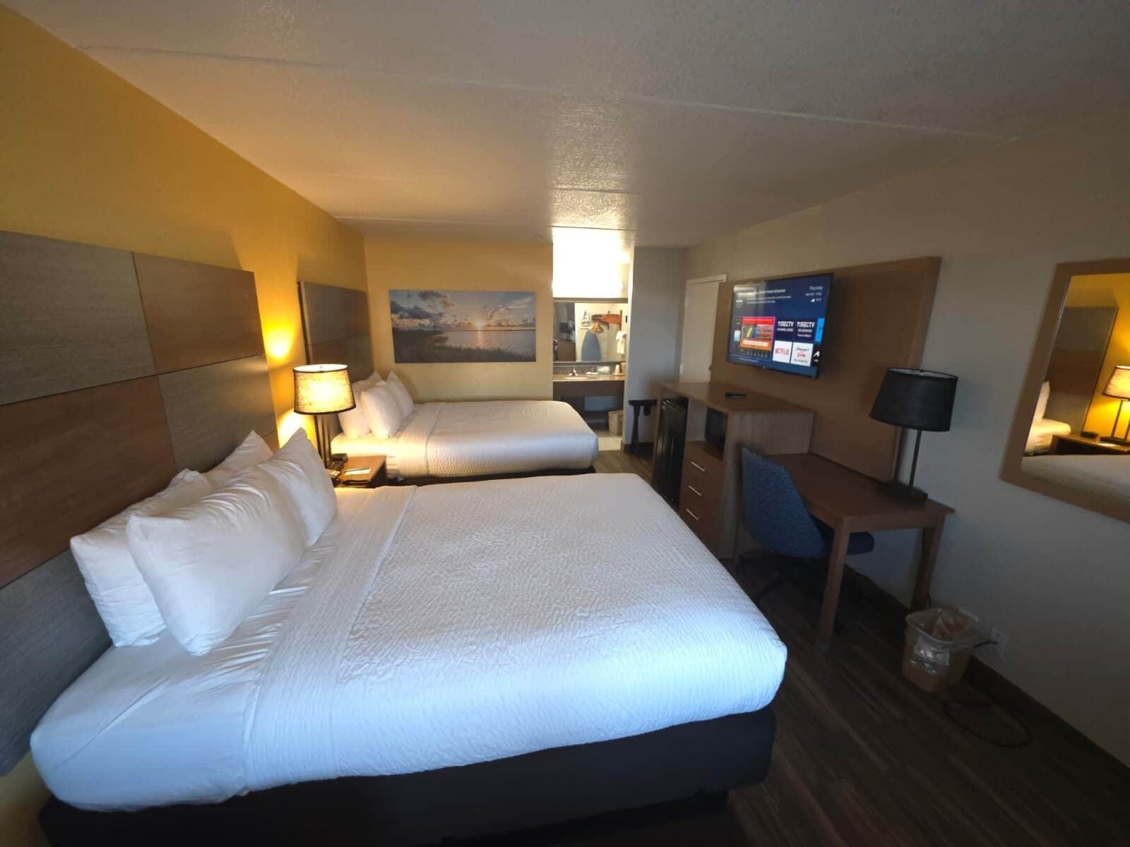 Habitación de hotel con dos camas, un escritorio, una silla, un televisor y un cuadro en la pared.