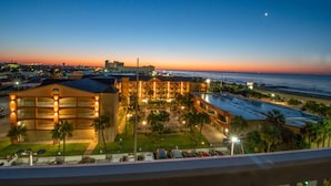 Un hotel de varios pisos, con estacionamiento y vista al océano al atardecer.