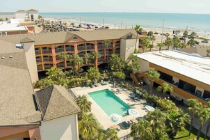 A hotel with a pool, palm trees, and a view of the beach.