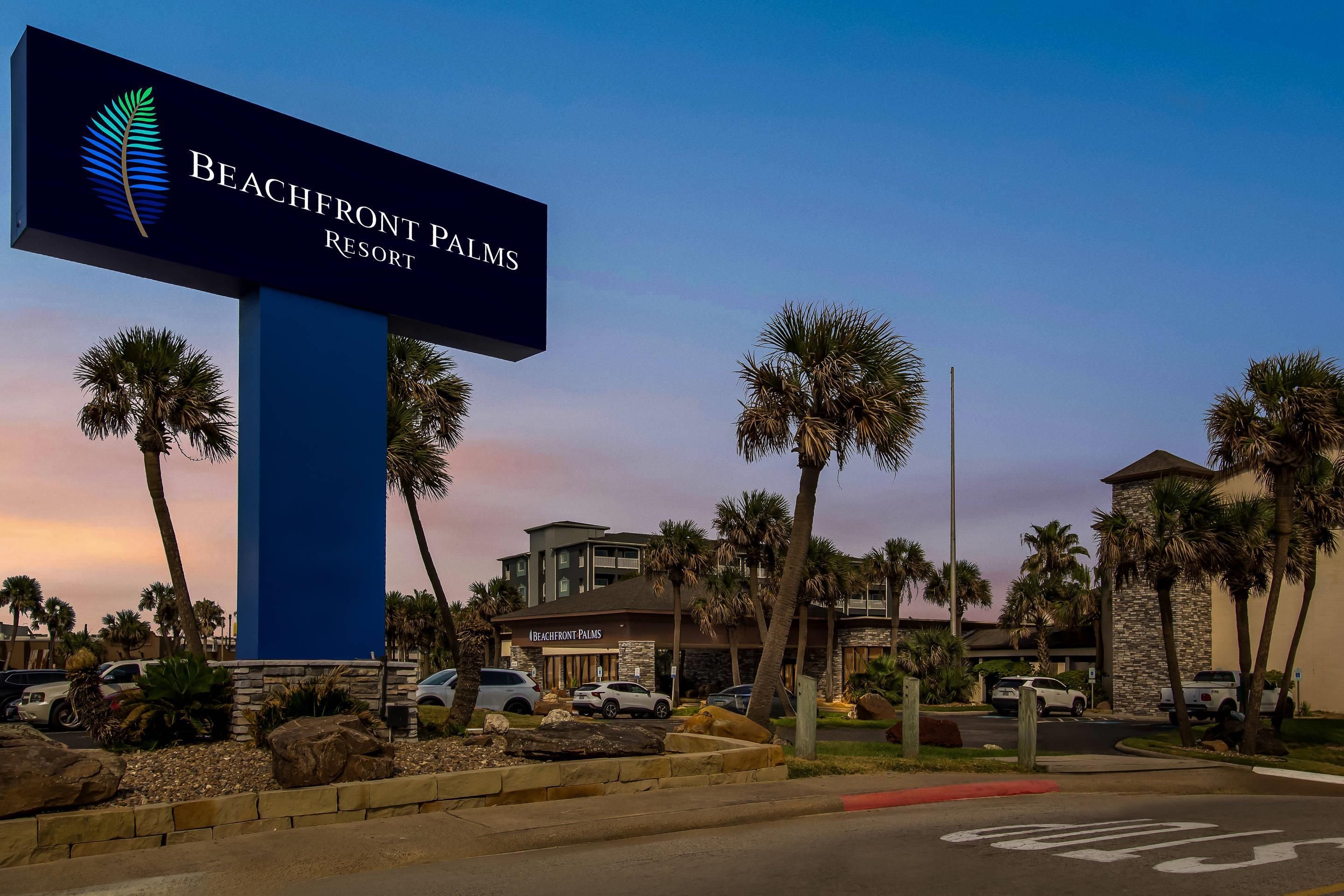 A sign for Beachfront Palms Resort with a modern building and palm trees in the background.