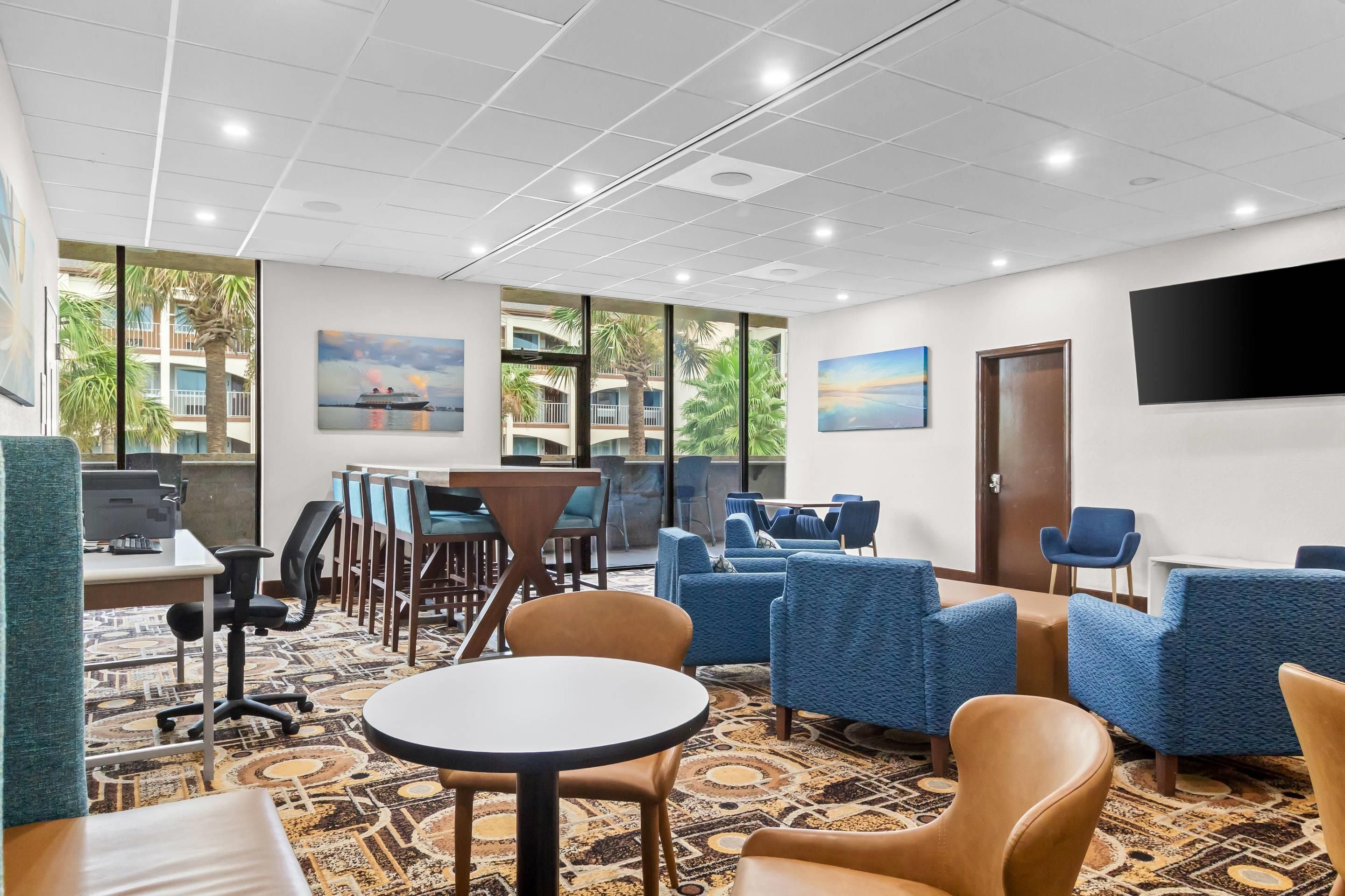 Habitación de hotel con escritorio, sillas, una mesa redonda, televisión y obras de arte en las paredes.