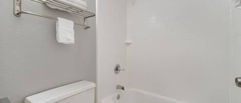 A bathroom with a toilet, a bathtub, and a towel rack with folded towels.