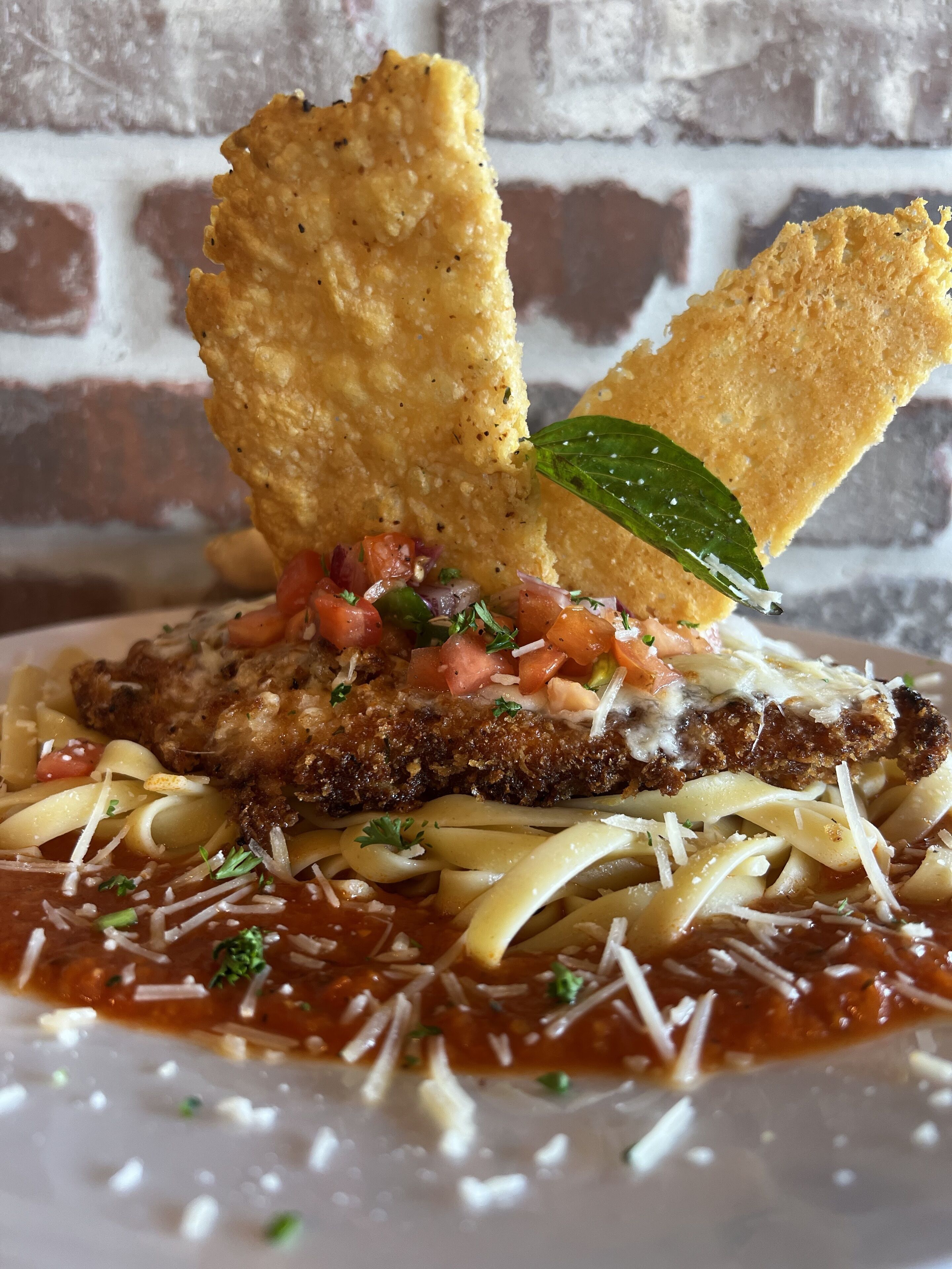 A plate of pasta with a breaded cutlet, tomato sauce, and grated cheese.